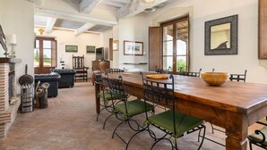Un comedor con una mesa de madera, sillas con cojines verdes y un cuenco grande de madera.