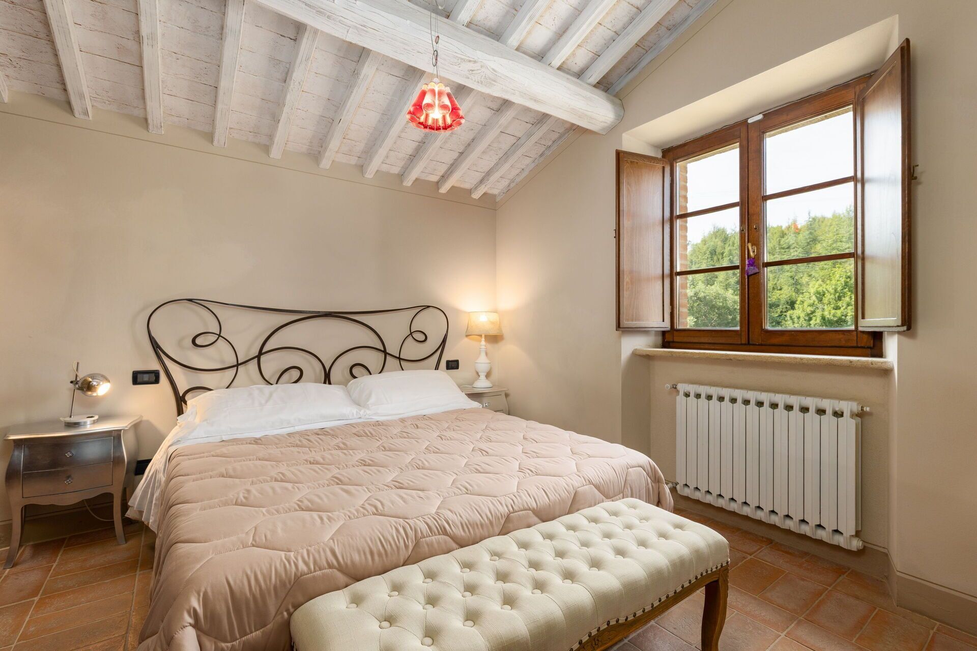 Une chambre à coucher comprenant un lit, une lampe de chevet, une fenêtre, un radiateur et un banc.