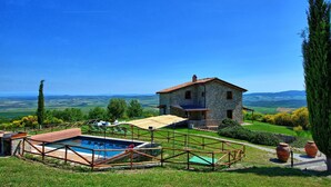 Una casa de piedra con piscina y mobiliario exterior, rodeada de vegetación y colinas.