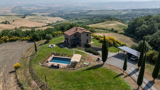 Una casa de piedra con techo de tejas rodeada de un césped cuidado y una piscina.