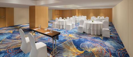 Un salón de conferencias con mesas redondas y sillas blancas, alfombra estampada y paneles de madera.
