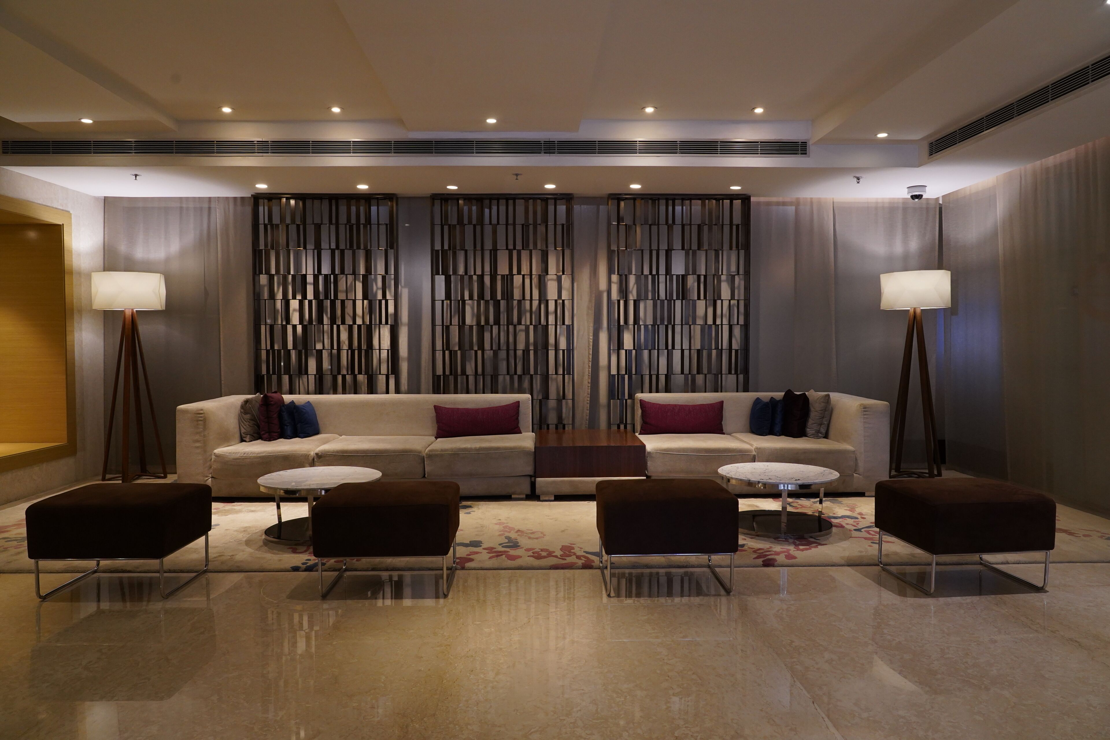 A modern lobby with a sofa, ottomans, and lamps.