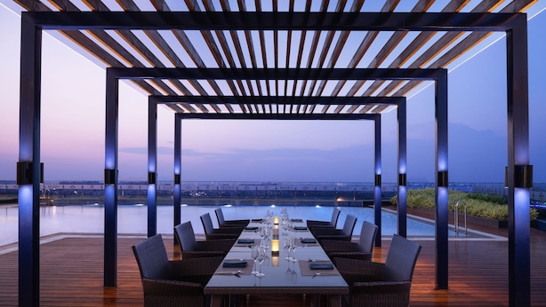 An outdoor dining area with a view of the water, wooden flooring, and a pergola structure. - Marriott Executive Apartments Hyderabad (Hyderabad)