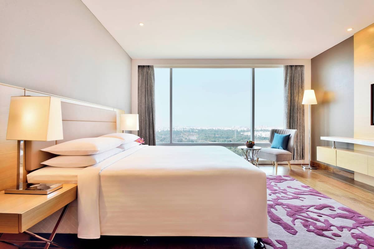 Ein modernes Hotelzimmer mit einem großen Bett, Nachttischlampen, Blick auf die Stadt, einem kleinen Tisch und einem Sessel.
