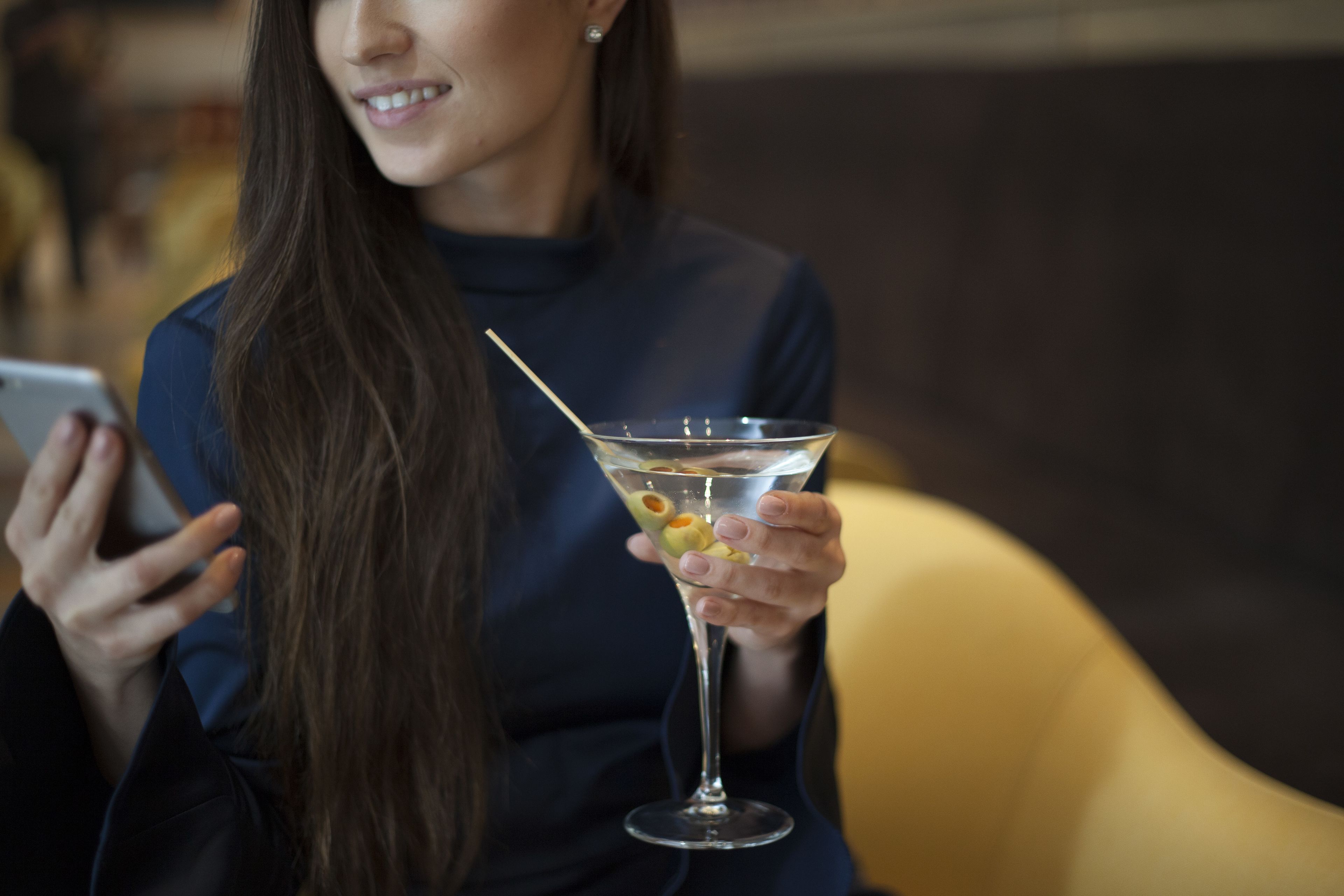 Une personne tenant un verre à martini garni d’olives et utilisant un téléphone intelligent.