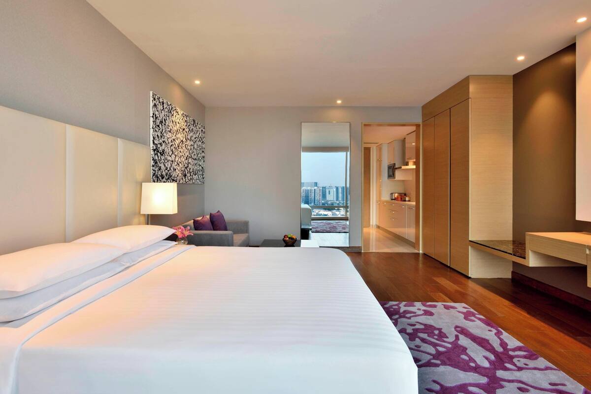 Ein modernes Hotelzimmer mit einem großen Bett, Blick auf die Stadt und einem begehbaren Kleiderschrank.