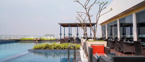 A rooftop pool area with a clear view of the city skyline, outdoor seating, and a covered seating area.