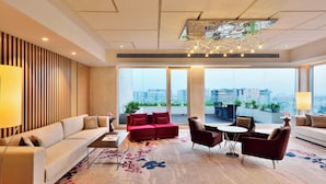 A modern living room with a sofa, armchairs, a coffee table, and a dining area. Large windows offer a view of the cityscape. - Marriott Executive Apartments Hyderabad (Hyderabad)