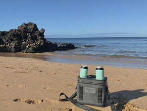 Un borsone YETI su una spiaggia sabbiosa con un promontorio roccioso sullo sfondo e mare calmo.