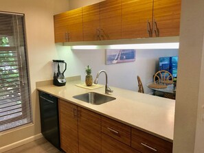 Una cucina moderna con mobili in legno, lavastoviglie integrata, frullatore, un'ananas sul bancone e un'area pranzo con una sedia e un tavolo.