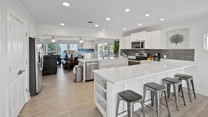 A modern kitchen with white cabinetry, a large island with bar stools, and a view to the living area. - Gorgeous Gulf View Home with Private Pool! Pet friendly too! (Pensacola Beach)