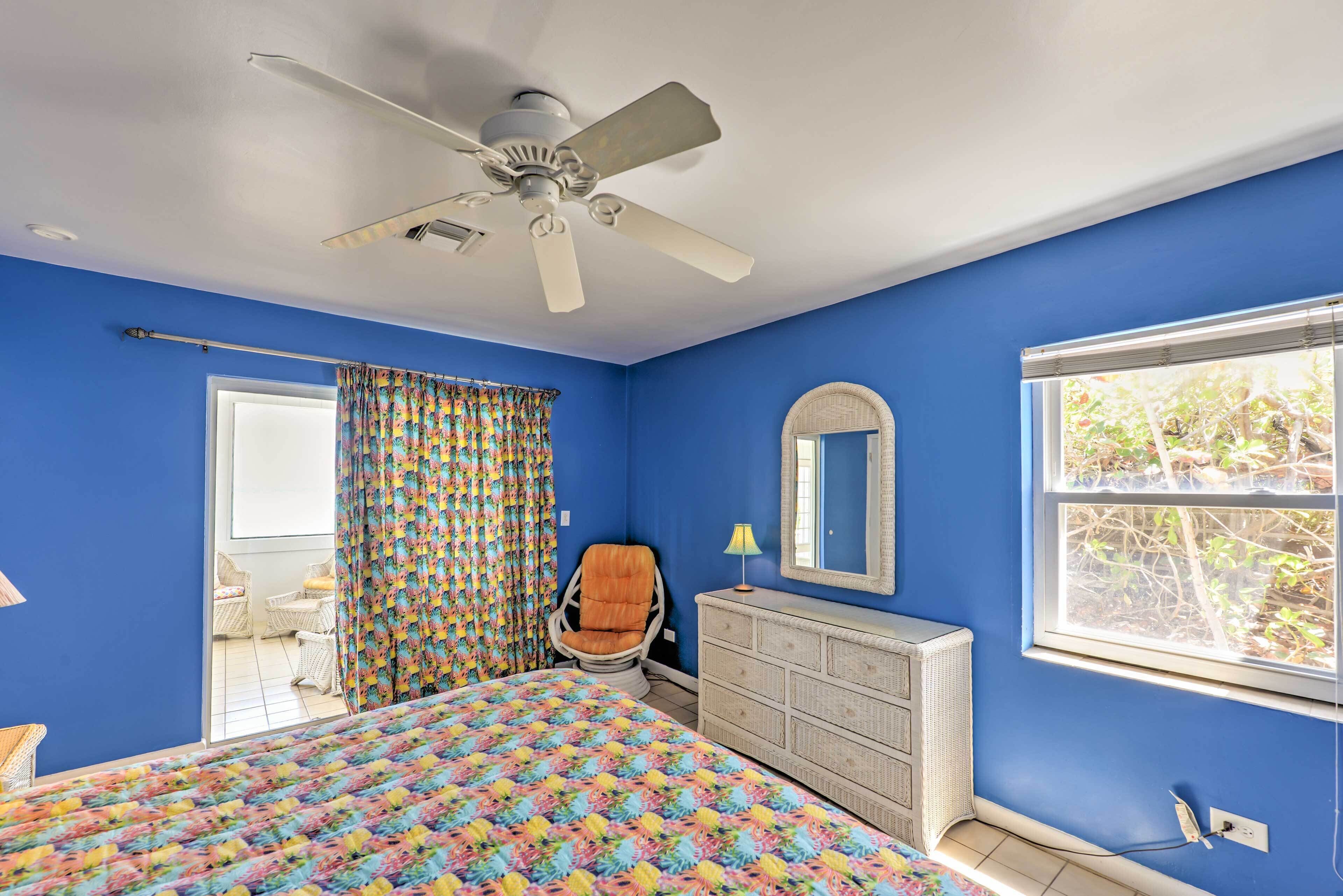 A bedroom with a bed, a dresser, a chair, a ceiling fan, a window, and a door leading to an outdoor area.