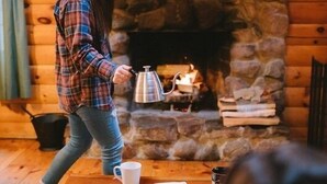 A cozy room with a stone fireplace, wooden walls, a table with a coffee pot, a mug, and a notebook.