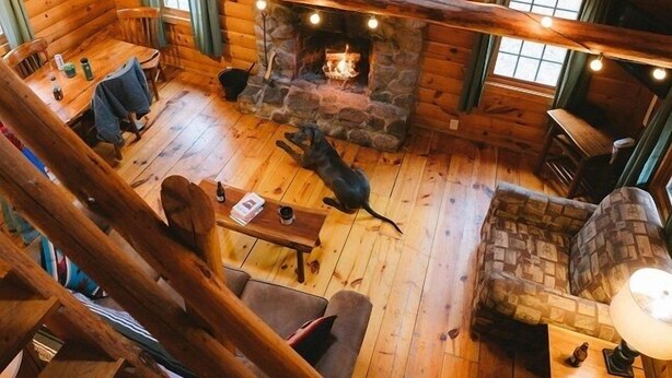 A cozy cabin interior with a stone fireplace, wooden walls, and a dining area.