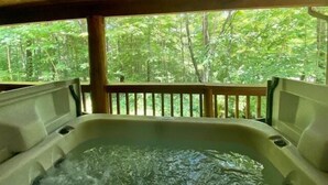 A hot tub with a wooden deck and a view of a forest.