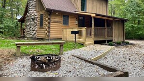 A log cabin with a stone chimney, a porch, and a fire pit.