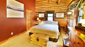 Une chambre à coucher située dans une cabane en rondins, avec un lit, une commode en bois, une table de chevet, une lampe et une fenêtre.