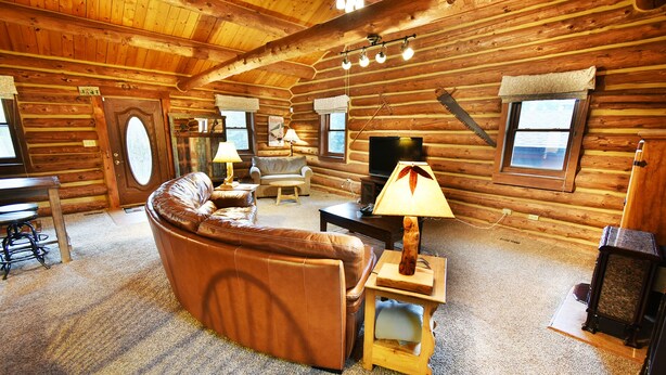 L’intérieur d’une cabane en rondins, avec un canapé en cuir, des tables en bois, un téléviseur et une cheminée.