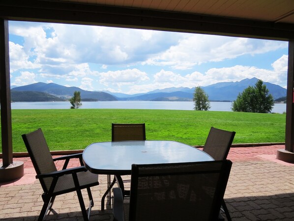 Relax in this serene outdoor seating area with a table and four chairs, taking in the breathtaking views of a body of water, a lush green field, and distant mountains.