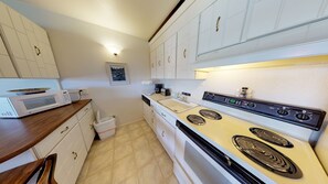 Features a stove with four burners and a microwave, along with white cabinets and a trash bin.