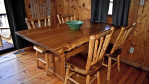 Une table à manger en bois avec des chaises, un saladier vert et une fenêtre avec des rideaux.