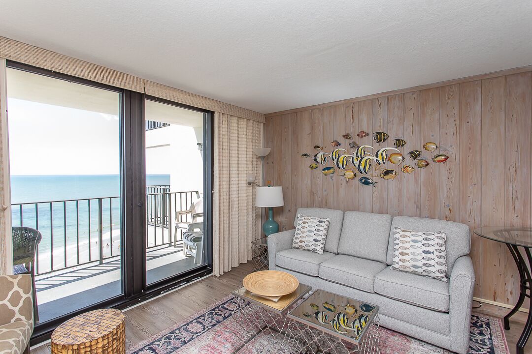 Ein Wohnzimmer mit einer Couch, einem Couchtisch und einem Wandbild von Fischen. Es gibt einen Balkon mit Meerblick.