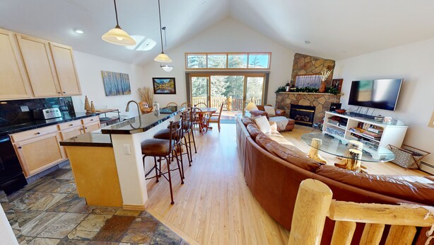 A spacious kitchen with a central island, a dining area with chairs, a living room with a sofa and TV, and a stone fireplace. - Private Hot Tub, Lift Chairs. On River Rec Trail. Easy Drive to Dine, Shop (Silverthorne)