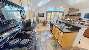 A modern kitchen with granite countertops, a built-in stove, and a dining area with wooden chairs. - Private Hot Tub, Lift Chairs. On River Rec Trail. Easy Drive to Dine, Shop (Silverthorne)