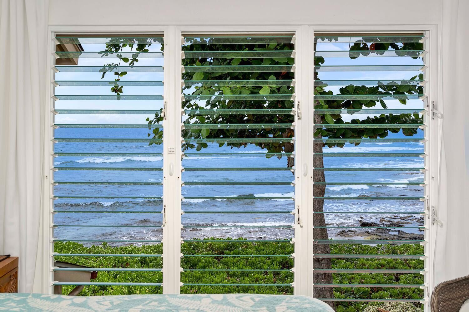 A room with a view of the ocean through a window with horizontal blinds.