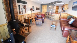 A cozy living room with a fireplace, a wooden dining area, and a kitchen in the background. - On Lake, Views! Hot Tub. Walk to Concerts, Marina, Dining. 1st Floor (Dillon)