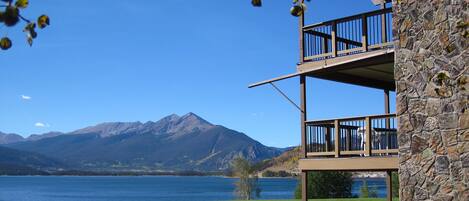 Un edificio de varios pisos con fachada de piedra y balcones con vistas a un lago y montañas.