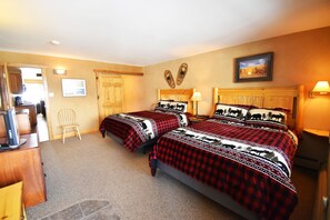 Quarto de hotel com duas camas, uma cabeceira de madeira, uma pequena mesa e uma cadeira.