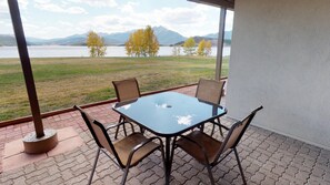 A patio with a table and chairs, overlooking a lake and mountains.