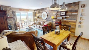 A cozy living room with a wooden dining table, leather sofa, and a large window offering a view of the outdoors. - On Lake! Updated! 1st Floor, Hot Tub. Walk to Amphitheater, Marina, Parks (Dillon)