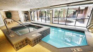 Een binnenzwembad met jacuzzi en een apart gedeelte voor kinderen, omgeven door grote ramen met uitzicht op het omliggende landschap.