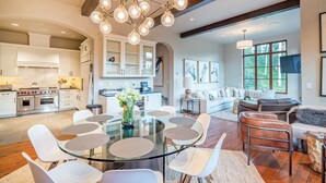 Une cuisine spacieuse dotée d’appareils électroménagers modernes, un coin repas avec une table en verre et un salon confortable avec une cheminée.
