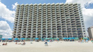 A high-rise hotel with multiple balconies, a sandy beach in front, and beach umbrellas. - Beachfront comfort with unforgettable views (Murrells Inlet)