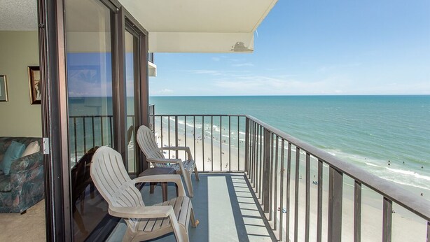 A balcony with a view of the beach, a glass door, and two chairs. - Beachfront comfort with unforgettable views (Murrells Inlet)