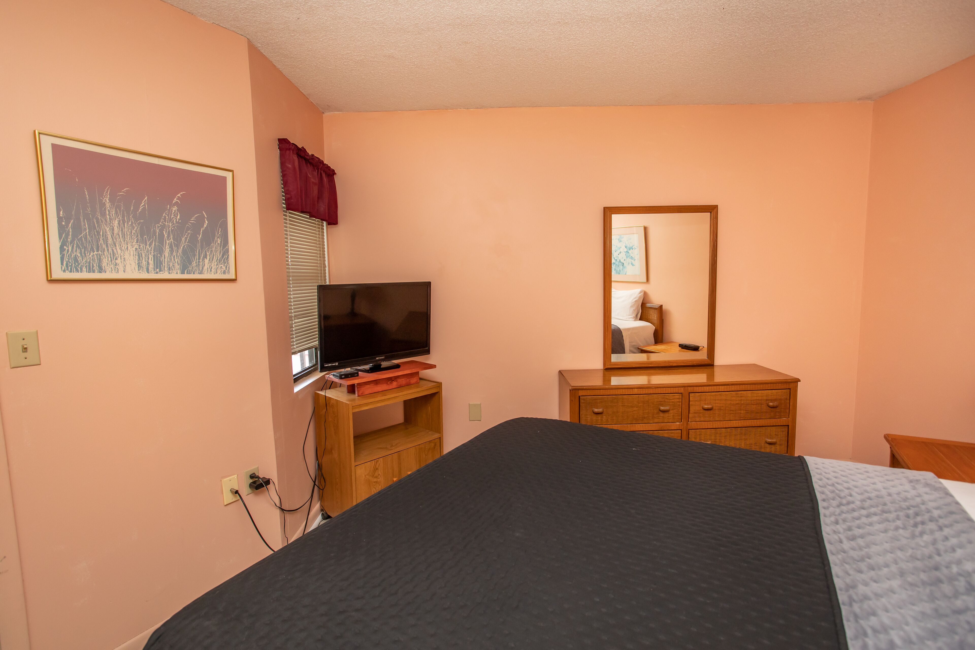 Een slaapkamer met een bed, een televisie op een houten standaard, een dressoir en een spiegel.