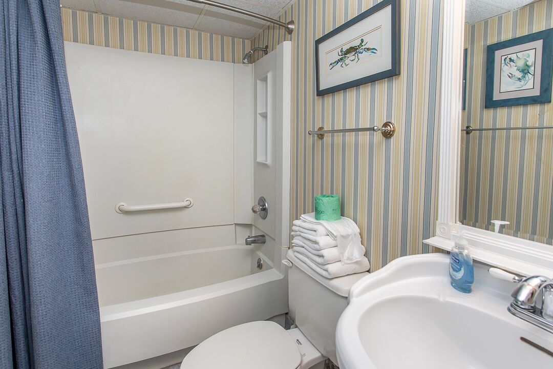 A bathroom with a bathtub, toilet, and sink. There are striped walls and framed artwork on the wall.