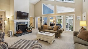 A spacious living room with a fireplace, a television, and a large window offering a view of the outdoors.