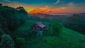 A rural house with a red roof, surrounded by lush green fields and trees, during sunset. - Deer Run - Hosted by The Chalets (Logan)