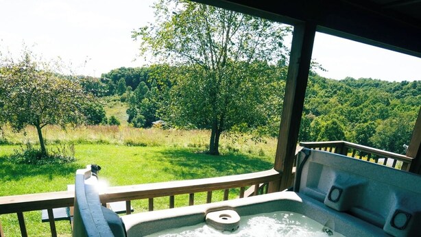 A hot tub on a wooden deck with a view of a green landscape. - Deer Run - Hosted by The Chalets (Logan)