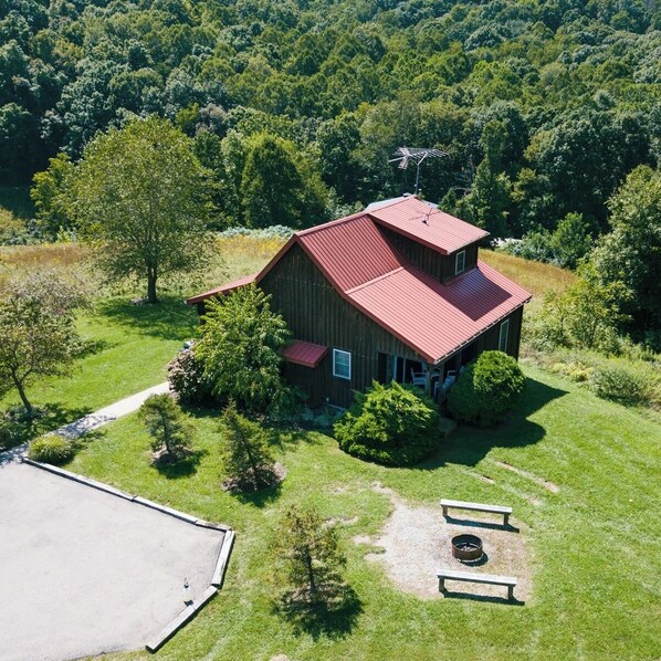 Une maison en bois à deux étages, avec un toit rouge, entourée d’une pelouse bien entretenue et d’arbres.