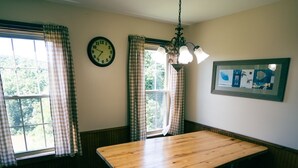 A dining area with a wooden table and benches, checkered curtains, a wall clock, and a framed picture. - Deer Run - Hosted by The Chalets (Logan)