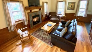 A spacious living room with a fireplace, a sofa, a chair, and a television mounted on the wall. - Deer Run - Hosted by The Chalets (Logan)