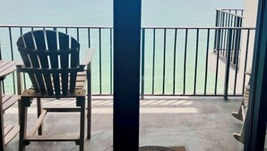 Un balcon avec vue sur l’océan, une chaise en bois et un sol en béton.
