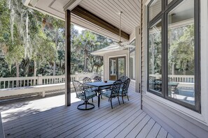Relax on the covered patio with a round table and six chairs, surrounded by lush greenery and trees.