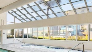 Piscina com teto de vidro, vista clara para o exterior e chão azulejado.