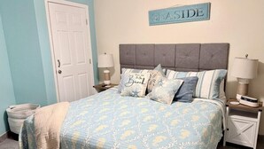 Quarto com cama, mesa de cabeceira, abajur, placa na parede e porta.